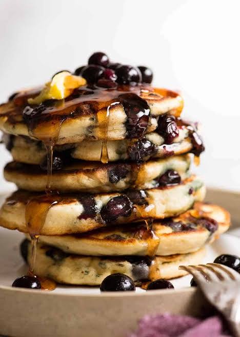 A tall stack of blueberry pancakes with syrup